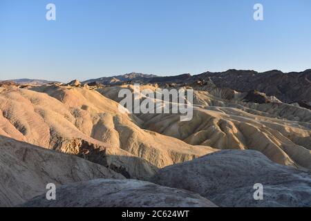 Tramonto con vista sui badlands dorati a Zabriskie Point nel Death Valley National Park, California. Le montagne della catena montuosa dell'Amargosa sono dietro. Foto Stock