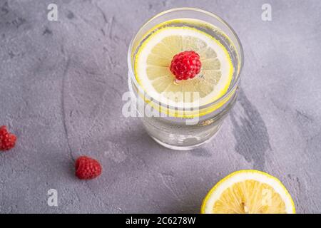 Bevanda fresca fredda con limone, frutta lampone in vetro su fondo di pietra in cemento, bevanda estiva dieta, macro angle view Foto Stock