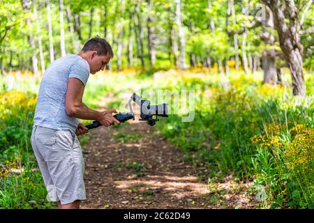 Storia del sentiero della foresta con il fotografo che si è fatto filmare tenendo gimbal in Shenandoah Blue Ridge appalachian montagne sullo skyline guidare giallo wildflo Foto Stock