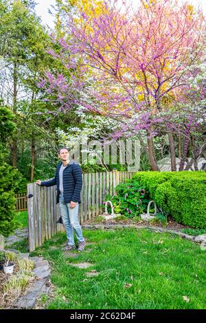 Giardino in Virginia con recinzione di legno e l'uomo apertura porta cancello da cespugli e dogwood bianco e fiori di primavera rosa rosso redbud su alberi Foto Stock