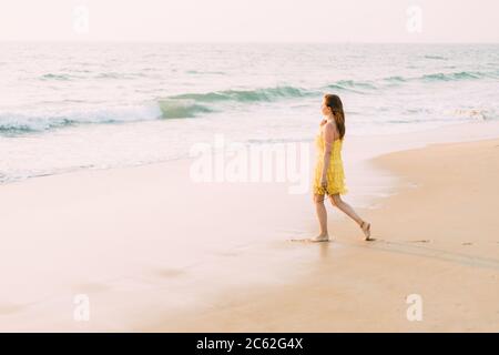 Goa, India. Giovane donna caucasica in abito giallo Vai al mare Oceano e guardando in lontananza Foto Stock