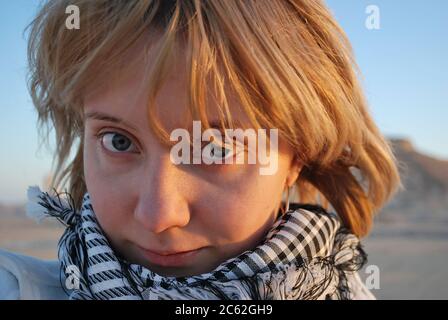 Primo piano ritratto della ragazza-viaggiatore bionda che indossa il suo modello di rete keffiyeh o sciarpa arabica kufiya nel deserto. Concetto di corsa estrema Foto Stock