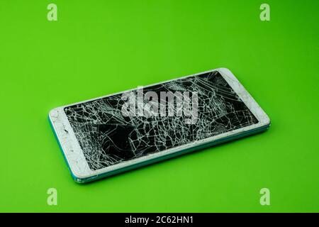 Lo schermo dello smartphone è incrinato su sfondo verde Foto Stock