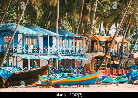 Canacona, Goa, India. Barca da pesca e famose Case ospiti dipinte sulla spiaggia di Palolem sullo sfondo delle palme Tall nel giorno del sole Foto Stock