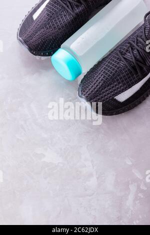 Concetto di fitness con sneakers e bottiglia d'acqua. Attrezzature sportive su sfondo grigio. Concetto di stile di vita sano. Spazio di copia. Vista dall'alto Foto Stock