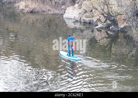 Vista dall'alto di sportivi addestrati che si trovano sulla tavola da paddle stand-up e che camminano sulle acque calme del fiume lungo la costa rocciosa. Uomo che paddling su SUP Foto Stock