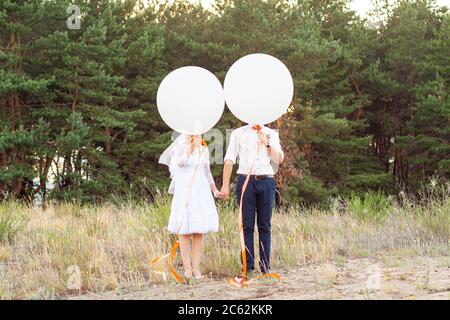 Sposa e sposo che tengono grandi berline di elio bianco con nastri di arancio nella foresta. Concetto di idea di matrimonio, sfondo Foto Stock