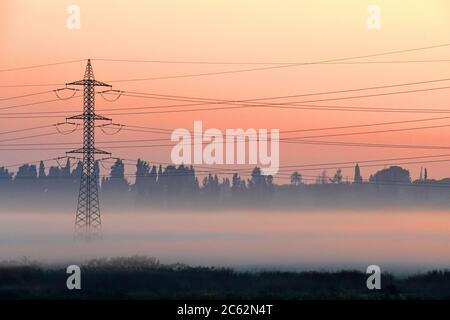 Torre di trasmissione che emerge dalla nebbia all'alba Foto Stock