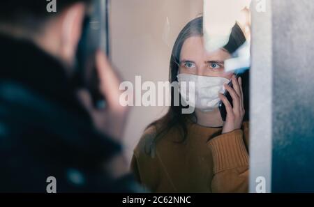 giovane coppia in maschere protettive guardandosi attraverso il vetro Foto Stock