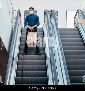 uomo in una maschera protettiva che si trova sulle scale mobili Foto Stock