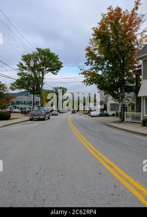 Vista di una strada americana quasi vuota vista entrare in una piccola città degli Stati Uniti con alcune auto lontane come visto all'inizio dell'autunno. Foto Stock