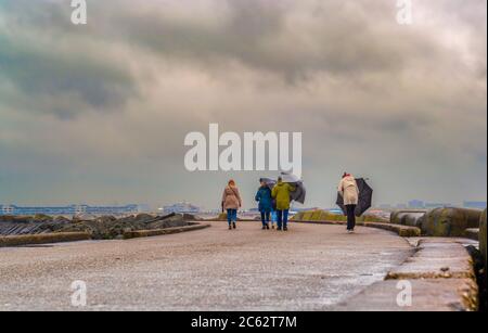 Un gruppo di persone che camminano e cercano di tenere gli ombrelloni in una giornata ventosa Foto Stock