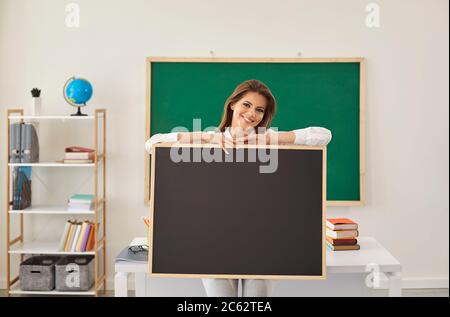 Giovane insegnante di sesso femminile che tiene una lavagna vuota con spazio per il tuo testo in classe. Buon tutor al lavoro. Ritorno a scuola Foto Stock