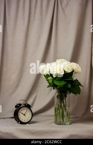 Bouquet di rose bianche in vaso e orologio su sfondo grigio Foto Stock