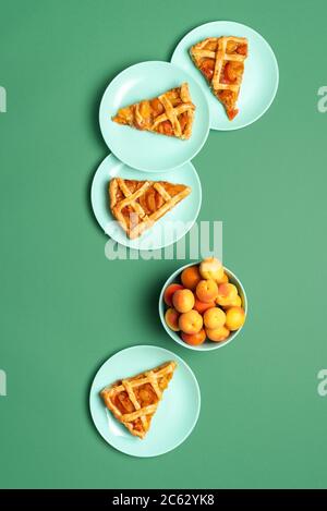 Fette di torta di albicocche con crosta a reticolo, su piatti verdi e fondo senza cuciture. Vista dall'alto del tavolo del Ringraziamento. Dessert estivo. Crostata fatta in casa. Foto Stock