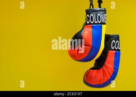 Replica guanti di boxe con etichetta Colombia e colori Country appeso di fronte a uno sfondo giallo chiaro. Concetto di combattimento con spazio di copia. Foto Stock