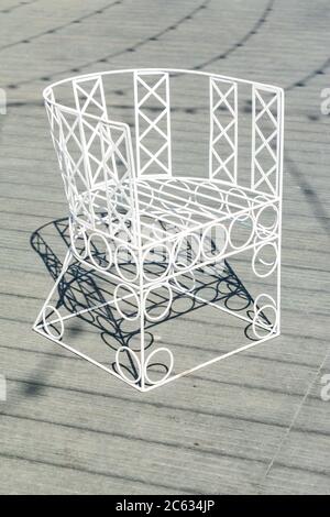 sedia forgiata in metallo bianco nel giardino su pavimento in legno grigio Foto Stock