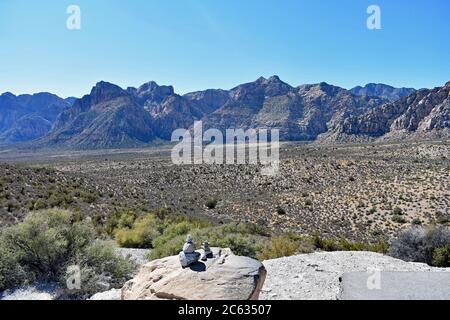 Red Rock Canyon visto dal punto alto si affaccia. Due piccole cairns roccia in primo piano con fogliame del deserto e montagne che si innalzano in lontananza Foto Stock