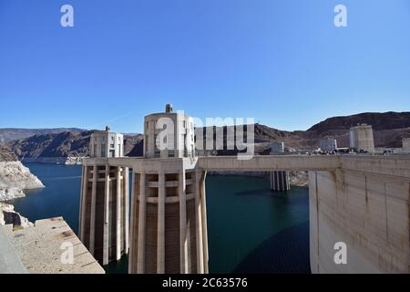 Le Torri di entrata della diga di Hoover viste dal lato del Nevada in una giornata limpida con cielo blu. I pedoni sono visibili camminando lungo la cima della diga. Foto Stock