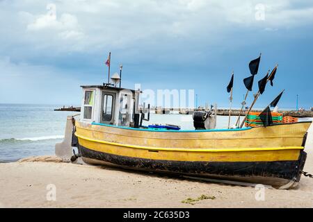 Vecchia e arrugginita barca da pesca e attrezzature sulla spiaggia sabbiosa, preparandosi per un viaggio di pesca. Pier e mare blu sullo sfondo, Niechorze, Polonia Foto Stock