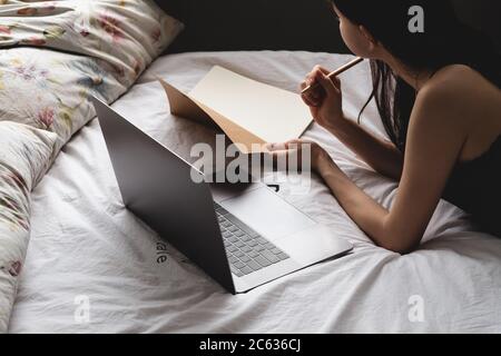 La giovane donna si trova sul letto con il laptop e il notebook. Foto Stock