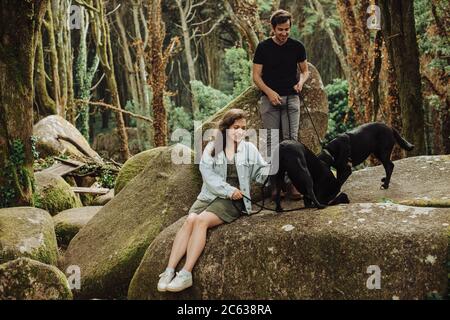 Giovane coppia con due cani che si divertono nella foresta mentre seduto sulla roccia Foto Stock