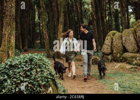 Coppia con cani su un guinzaglio sorridente l'uno all'altro, camminando nella foresta Foto Stock