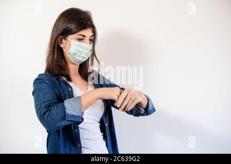 Donna con maschera di protezione medica che mette su antisettico per disinfettare le mani Foto Stock