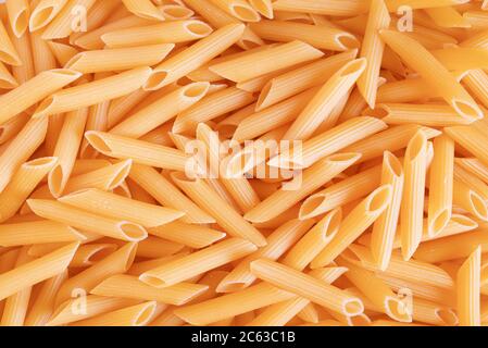 Penne pasta di fondo. Penne organiche grezze. Pasta tradizionale italiana di penne. Cucina italiana. Penne secche non cotte. Vista dall'alto. Tono caldo. Foto Stock