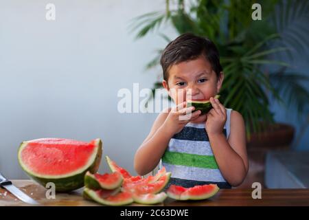 Ragazzo giovane che prende un morso da una fetta di anguria che tiene in bocca durante l'estate. Foto Stock