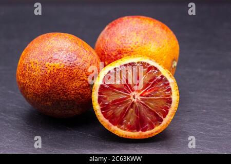 Piena e metà delle arance rosse isolate su sfondo scisto nero. Le citruse giacciono su una superficie di pietra Foto Stock