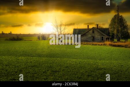 Antico casale in campo al tramonto con mulino a vento, Foto Stock