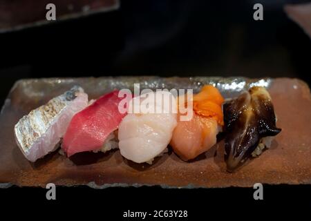 Il set di sushi premium è collocato su una piastra di pietra nera. Vista dall'alto, immagine a toni scuri. Foto Stock