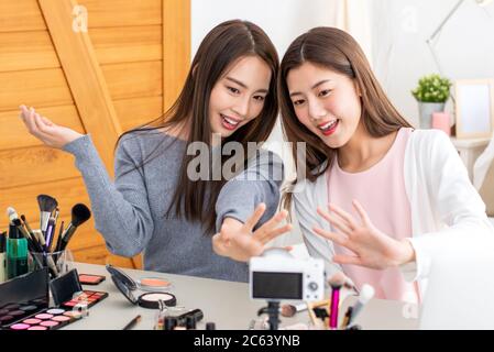 Bella ragazza asiatica amico bellezza influencers agitando le mani al pubblico durante la registrazione di video virale con la fotocamera a casa Foto Stock