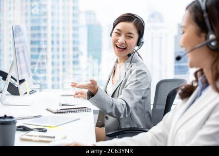 Sorridente bella donna asiatica telemarketing agente di servizio clienti in ufficio centrale di chiamata parlare con collega Foto Stock