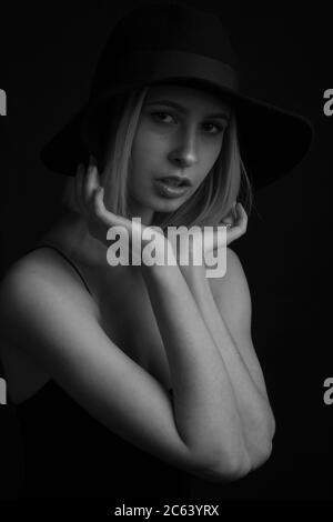 Nero e bianco ritratto bionde su uno sfondo nero in un cappello e canotta Top con sottili cinghie. Le mani delle persone Foto Stock