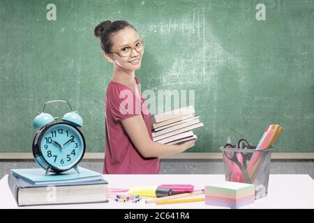 Donna studentesca asiatica che porta una pila di libri in classe. Concetto di ritorno a scuola Foto Stock