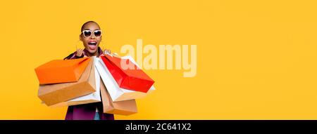 Bella donna afro-americana alla moda con borse colorate in vendita sorpresa concetto isolato su sfondo giallo banner Foto Stock