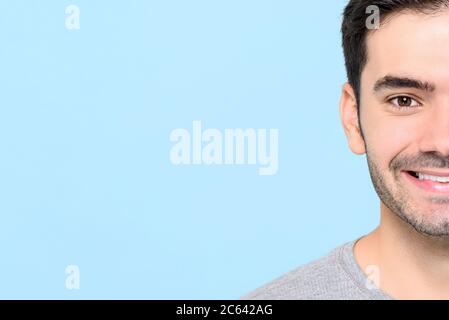 Metà faccia in primo piano di un giovane bel ragazzo caucasico sorridente isolato su sfondo azzurro con spazio di copia Foto Stock