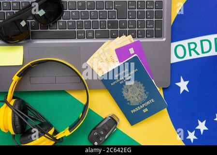 Vista dall'alto degli oggetti da viaggio: Passaporto brasiliano, notebook, occhiali da sole, chiavi, carta di credito, blocco note, penna, denaro e bandiera brasiliana sullo sfondo. Tra Foto Stock