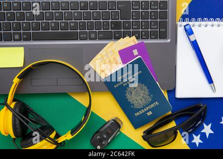 Vista dall'alto degli oggetti da viaggio: Passaporto brasiliano, notebook, occhiali da sole, chiavi, carta di credito, blocco note, penna, denaro e bandiera brasiliana sullo sfondo. Tra Foto Stock