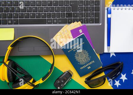 Vista dall'alto degli oggetti da viaggio: Passaporto brasiliano, notebook, occhiali da sole, chiavi, carta di credito, blocco note, penna, denaro e bandiera brasiliana sullo sfondo. Tra Foto Stock