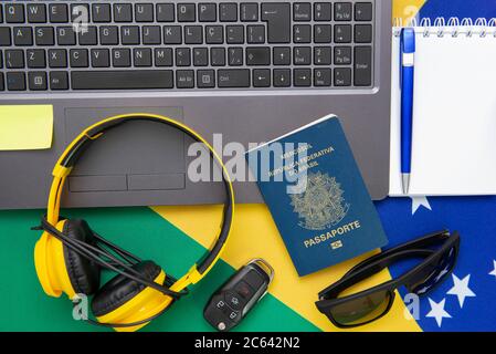 Vista dall'alto degli oggetti da viaggio: Passaporto brasiliano, notebook, occhiali da sole, chiavi, carta di credito, blocco note, penna, denaro e bandiera brasiliana sullo sfondo. Tra Foto Stock