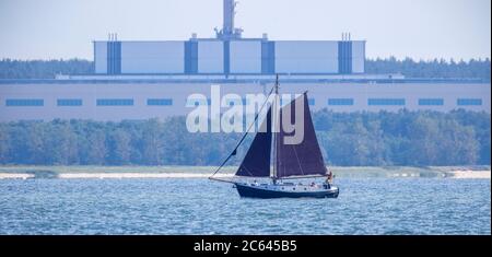 Lubmin, Germania. 02 luglio 2020. Una barca a vela sta navigando sul Greifswalder Bodden di fronte alla ex sede DI 'VE Kombinat Kernkraftwerke Bruno Leuschner'. Quando la centrale elettrica fu chiusa nel 1990 e i lavori di costruzione degli ultimi due blocchi furono interrotti, anche il complesso edilizio lungo 126 metri e alto 50 metri divenne un orfano. Il cumulo nucleare di Lubmin era destinato a rendere la RDT autosufficiente nelle importazioni di elettricità. Credit: Jens Büttner/dpa-Zentralbild/ZB/dpa/Alamy Live News Foto Stock