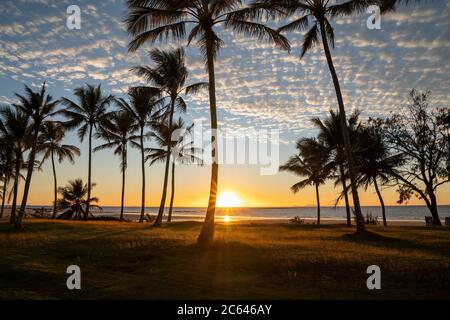 Il sole arancione si alza appena sull'orizzonte sulla costa australiana sotto un bel cielo blu nuvoloso Foto Stock