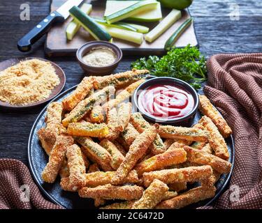 Grissini croccanti di zucchine impanati con panko, parmigiano, spezie su un piatto con ketchup, sano spuntino estivo con stuzzichini, vista da a. Foto Stock