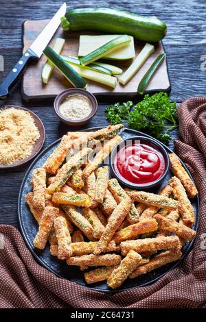 Bastoncini di zucchine croccanti impanati con panko pangrattato, parmigiano, spezie su un piatto con ketchup, sano spuntino estivo con stuzzichini, vi verticale Foto Stock