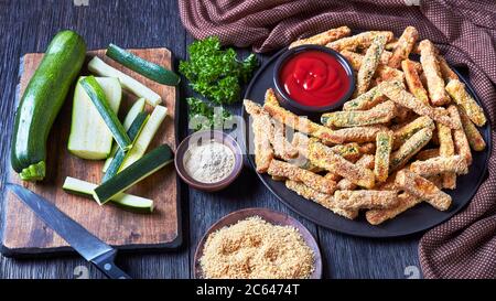 bastoncini di zucchine croccanti impanati con panko, parmigiano, spezie su un piatto nero con ketchup su un tavolo di legno, vista dall'alto, clos Foto Stock