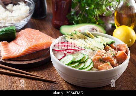 Poke Bowl, tradizionale insalata di pesce grezzo hawaiano con riso, avocado, cetriolo e rafano su sfondo di legno Foto Stock