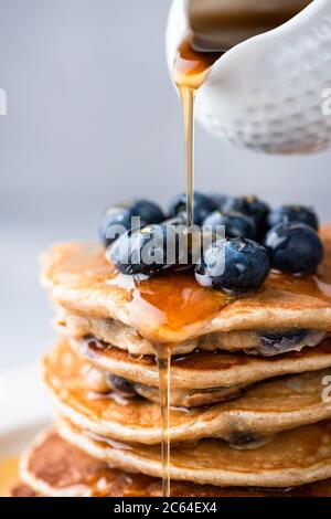 Sciroppo d'acero che si versa su una pila di pancake vista closeup. Sciroppo d'acero dorato dolce che si versa su frittelle di mirtillo Foto Stock